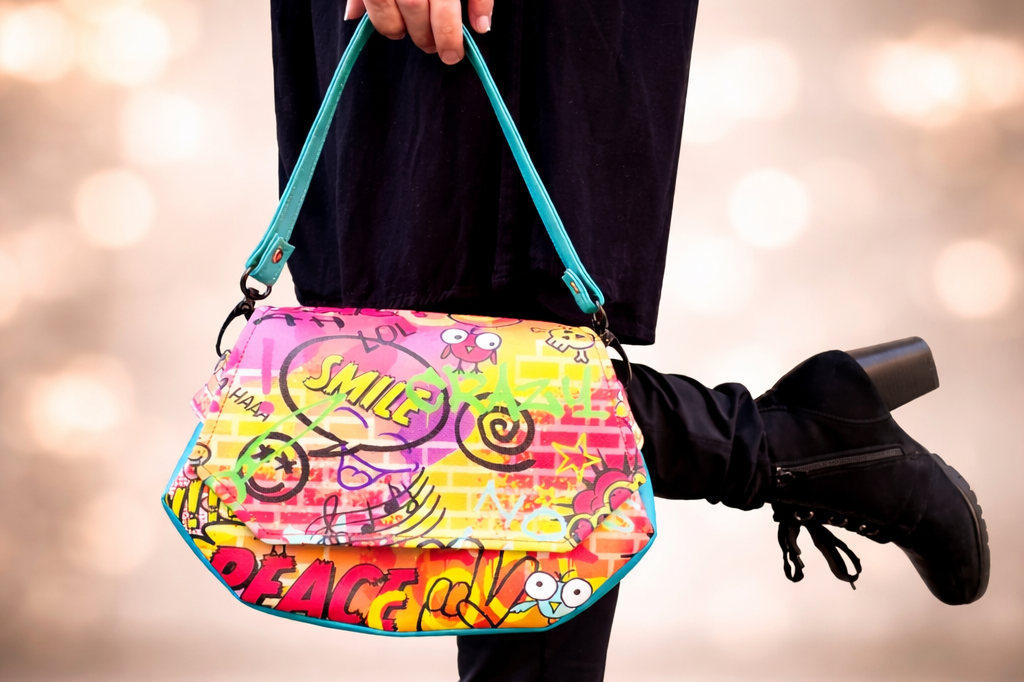 handgefertigte Taschen und Accessoires Farbige Umhängetasche mit Graffiti-Muster, schwarzer Stiefel auf einem Holzuntergrund.